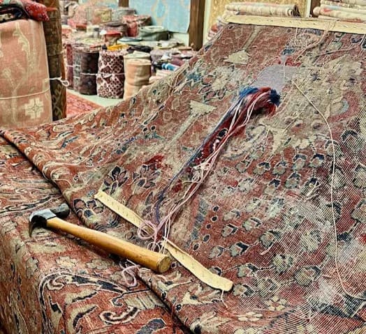Oriental rug on a restoration bench with yarns, a hammer, and a straightedge